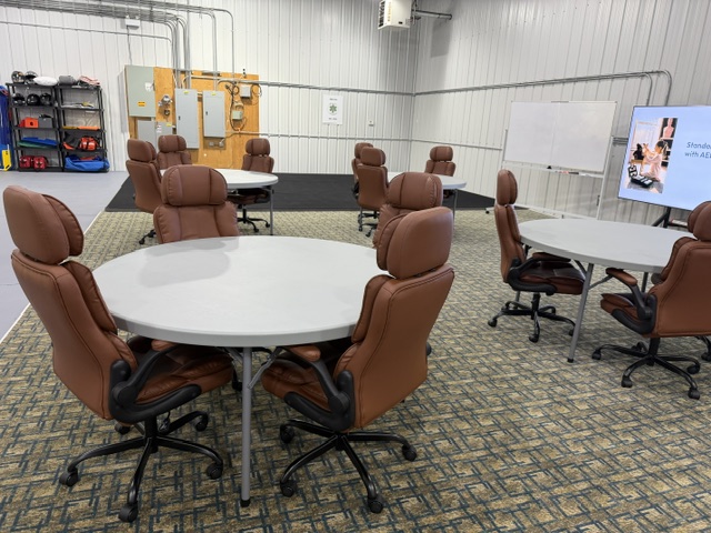 Sharalife classroom with round training tables, rolling chairs, equipment shelves, and presentation screen