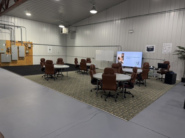 Wide Sharalife training classroom with round tables, whiteboard, and digital presentation display